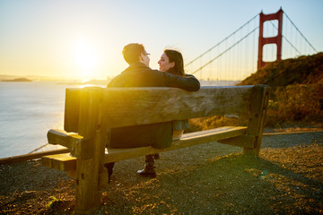 happy couple sitting on bench to watch the sun rise at the golden gate bridge