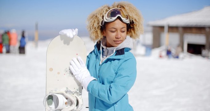 Happy friendly young woman with a cute afro hairstyle posing with a snowboard at a ski resort in white winter snow