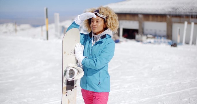 Attractive young woman posing at a winter ski resort in her ski clothes holding her snowboard and smiling at the camera  with copy space