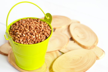 A small green bucket with raw buckwheat on a Board and a white wooden background