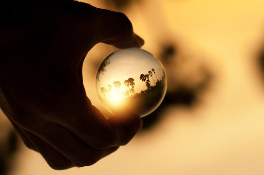 Hand Holding Glass Ball With Nature On Sunset Background