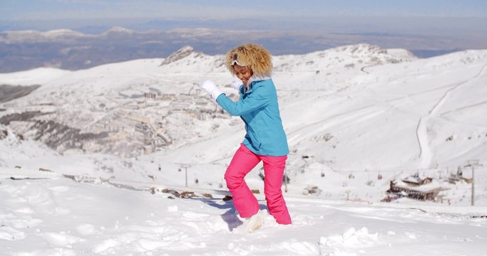 Single cute young adult in skiing clothes kicking snow at top of ski hill with mountain in background during sunny day