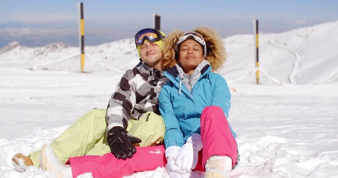 Attractive young man and woman in skiing outfits sitting in the snow on mountain after a busy day on the slope