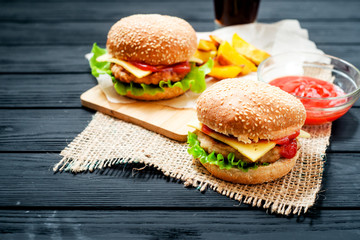 food, fast food, burgers with cheese , meat patty , lettuce, sauce , Baked potatoes and a drink , cola or beer on a wooden background