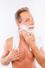 Handsome happy man with towel smearing shaving foam on his chin