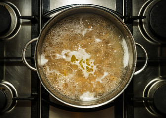Metal cooking pan with boiling water and wholewheat penne pasta on a stove