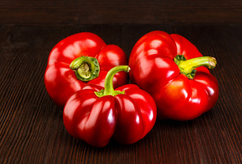 Three red peppers with green stems on dark wooden surface