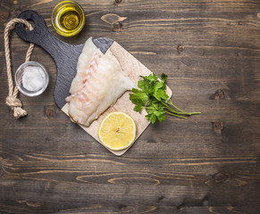 Raw fish fillet on a cutting board with lemon, herbs, butter and salt border ,place for text on wooden rustic background top view close up