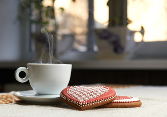 Steaming love. Cup of coffee steaming on the table heart shaped glazed cookies lying near