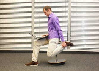 leg exercise during office work -  man on pneumatic stool, working with laptop in his office
