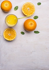 freshly squeezed juice from oranges in a glass with a straw, spread out around the oranges and mint on wooden rustic background top view close up