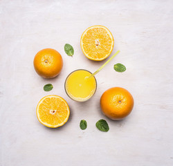 freshly squeezed juice from oranges in a glass with a straw, spread out around the oranges and mint on wooden rustic background top view close up