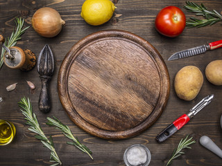 lemons, tomatoes, onions, potatoes, rosemary, knife for peeling potatoes laid out around a round cutting board place for text,frame on wooden rustic background top view close up