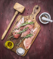 Crude appetizing chicken breast with rosemary, butter and salt on vintage cutting board with a hammer for meat Healthy food on wooden rustic background top view close up