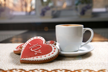 Sunny morning. Shot of a cup of warm coffee with heart shaped red cookie on the table in sunlight beams