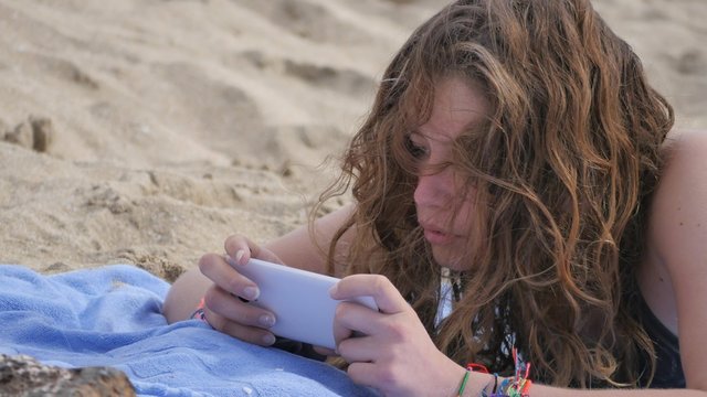 belle adolescente jouant au portable sur la plage