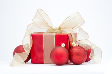 A red Christmas present with gold ribbon and red tree decoration