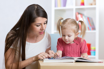 Young mother is reading a book to her child daughter.