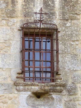 Medieval mullioned window with an ornate wrought iron security grill.
