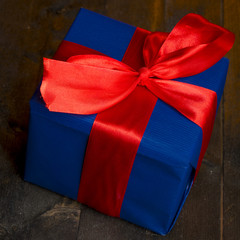 pacco regalo blu con fiocco rosso su sfondo legno