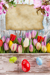 Colorful tulips with easter eggs on wooden table.