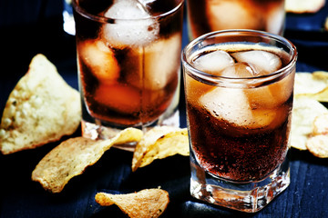 Cold Cola with ice in glasses and potato chips on a dark backgro