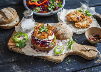 Obraz na płótnie Canvas Make fish burger. Ingredients - rye buns, red cabbage, peppers, carrots, herbs and crispy fried fish cutlets on a dark wooden background. Delicious food, rustic style