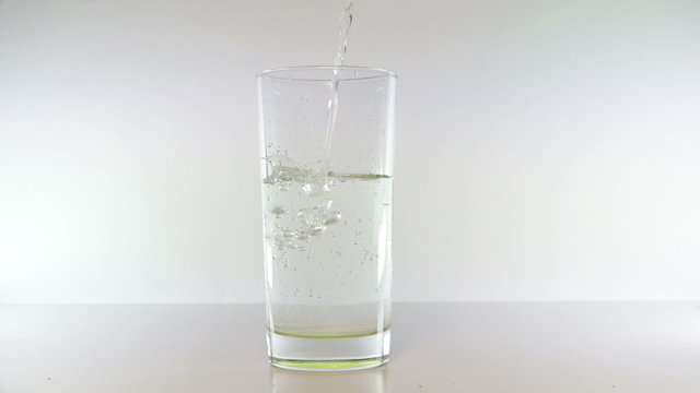 The stream of water pours from the top and fills a clear glass with water