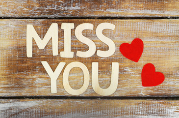 Miss you written with wooden letters on rustic surface and two red hearts
