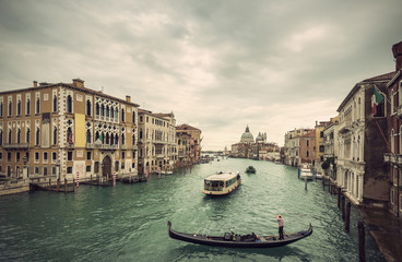 Fototapeta premium View of traditional Gondola and boats on Canal Grande with Basilica di Santa Maria della Salute church in background at a cloudy day, Venice (Venezia), Italy, Europe, Vintage filtered style 
