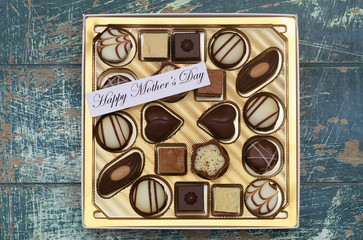 Happy Mother's Day card with box of assorted chocolates on rustic surface
