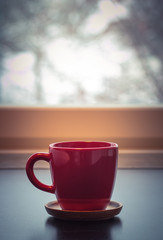 Red coffee tea mug cup in front of a window in a winter day 