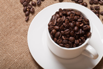 Cup, saucer and coffee beans on a burlap background. Selective f
