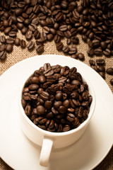 Cup, saucer and coffee beans on a burlap background. Selective f