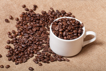 Cup, saucer and coffee beans on a burlap background. Selective f