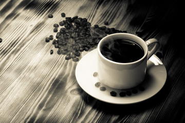 Coffee beans and coffee in white cup on wooden table. Selective