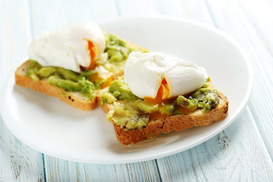 Poached eggs with avocado on toasts on blue wooden table