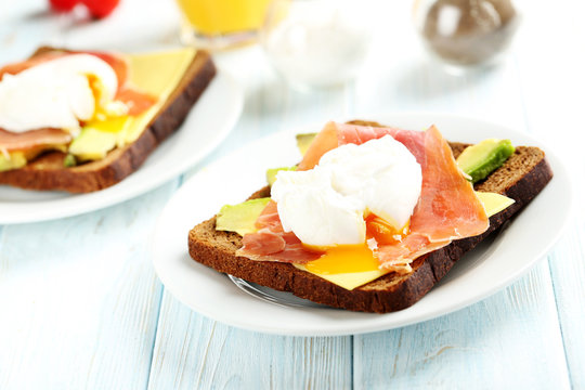 Poached eggs with avocado and bacon on toasts on blue wooden tab