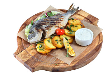 Fried fish dorade on wooden board with parchment and potatoes.
