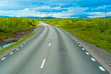 Fototapeta na wymiar Grey sweden road to Norvegian mountains in sunny summer day