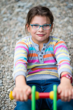 Funny girl in eyeglasses playing at children playground