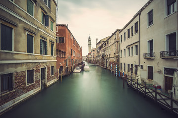 Long time exposure of canal in Venice (Venezia) with old buildings, boats and the leaning belfry tower of San Giorgio dei Greci, Italy, Europe, vintage filtered style
