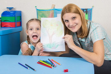 Five-year girl and the teacher happily show drawn on a sheet of wood