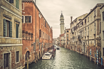 Fototapeta na wymiar Canal in Venice (Venezia) with old buildings, boats and the leaning belfry tower of San Giorgio dei Greci, Italy, Europe, vintage filtered style 