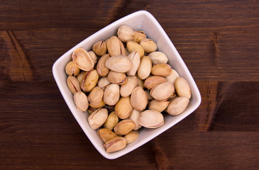 Pistachios on a square bowl on wooden table seen from above