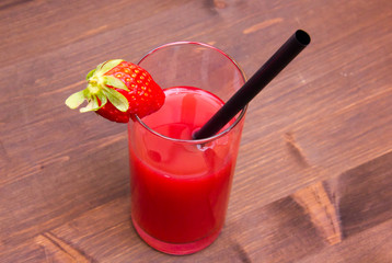 Glass with strawberry juice on wooden table seen from above