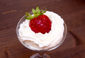 Glass with strawberry and cream on wooden table seen up close