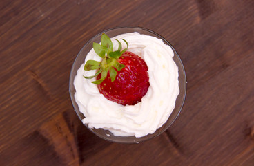 Glass with strawberry and cream on wooden table seen from above