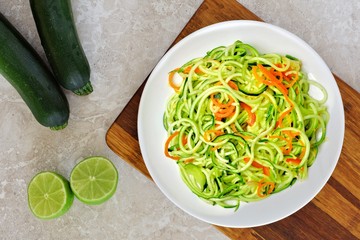 Low carb zucchini noodle dish with carrots and lime on white marble background, overhead view