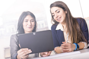 Young successful business women discussing and sharing ideas, using tablet in bright modern office. Focus on girl on the right